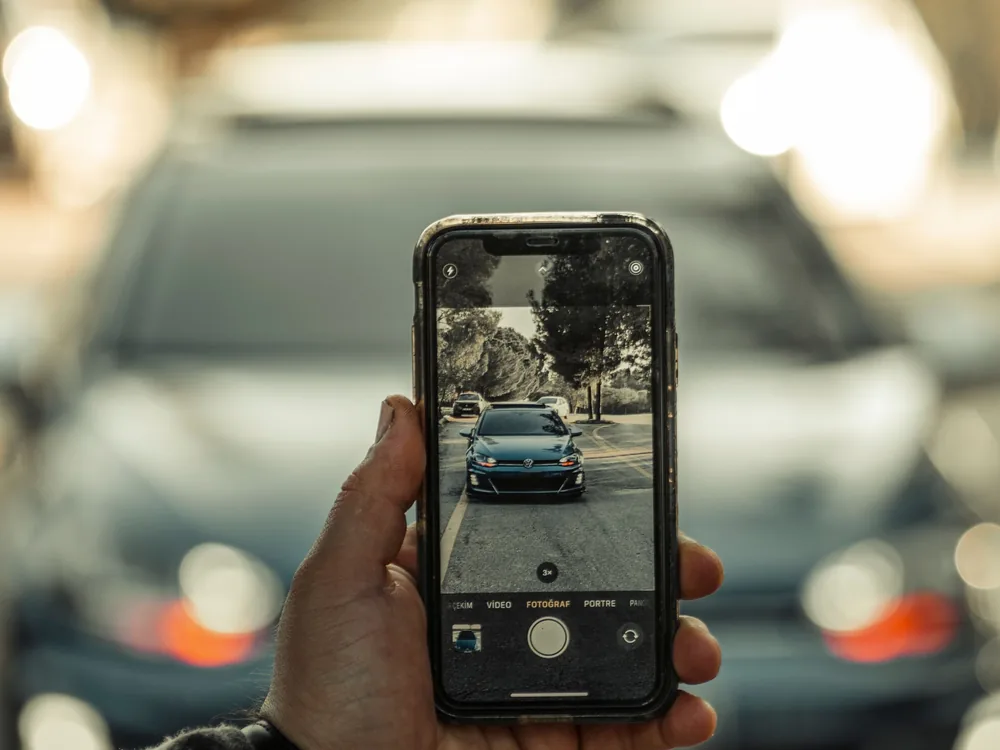 Kéz mobiltelefonnal fényképez egy autót, a kijelzőn látszik a kép